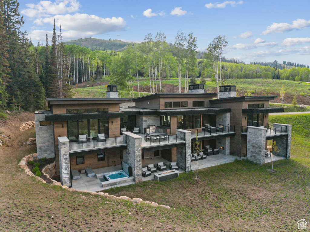 Rear view of house with a patio, stone siding, an outdoor hangout area, a balcony, and a forest view