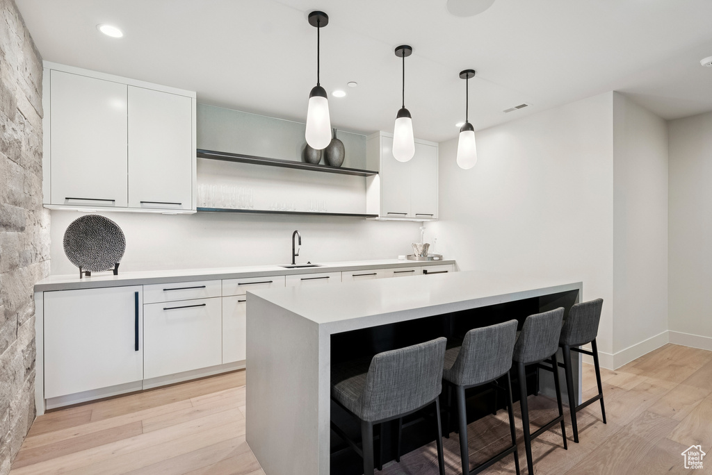 Kitchen with light wood-style floors, light countertops, white cabinets, a breakfast bar area, and recessed lighting