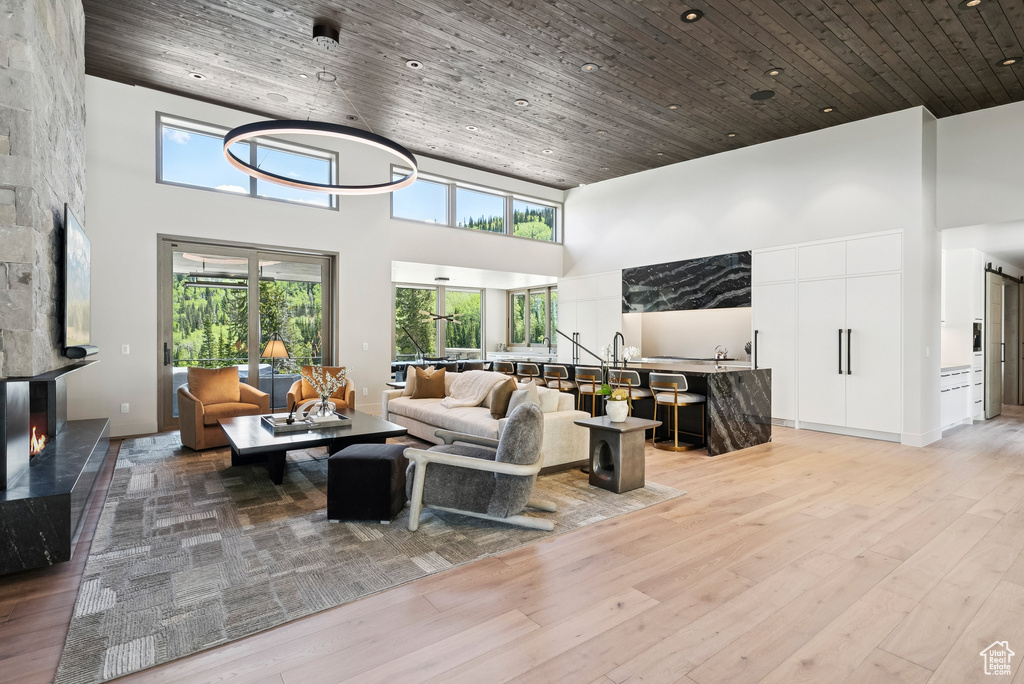 Living area featuring a high ceiling, plenty of natural light, light wood finished floors, wooden ceiling, and a premium fireplace