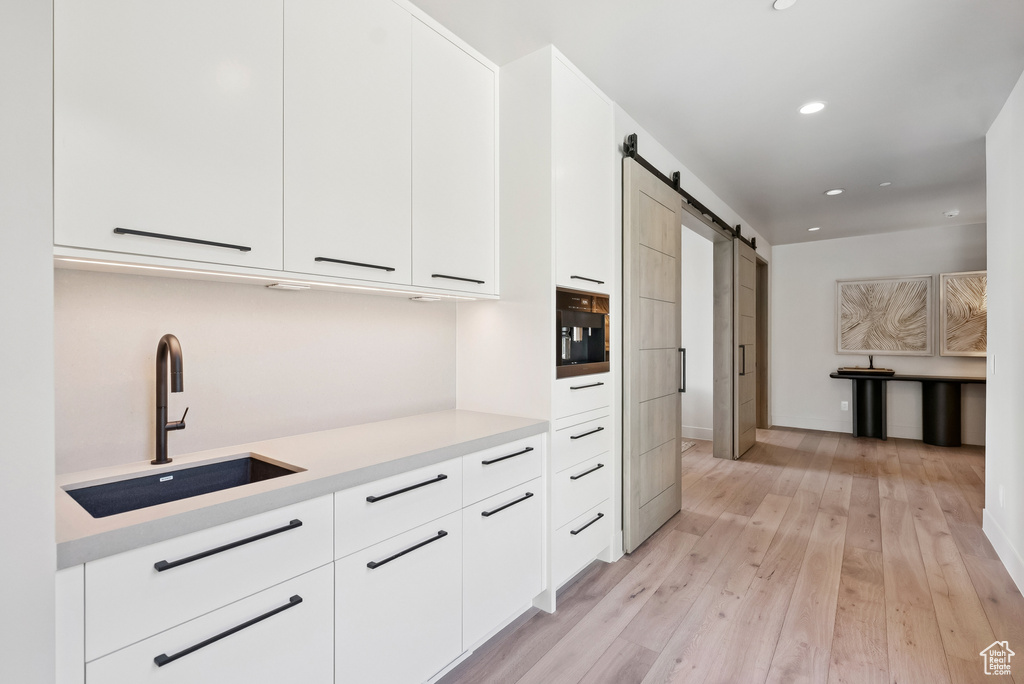Kitchen with a barn door, light wood-style flooring, white cabinets, modern cabinets, and recessed lighting
