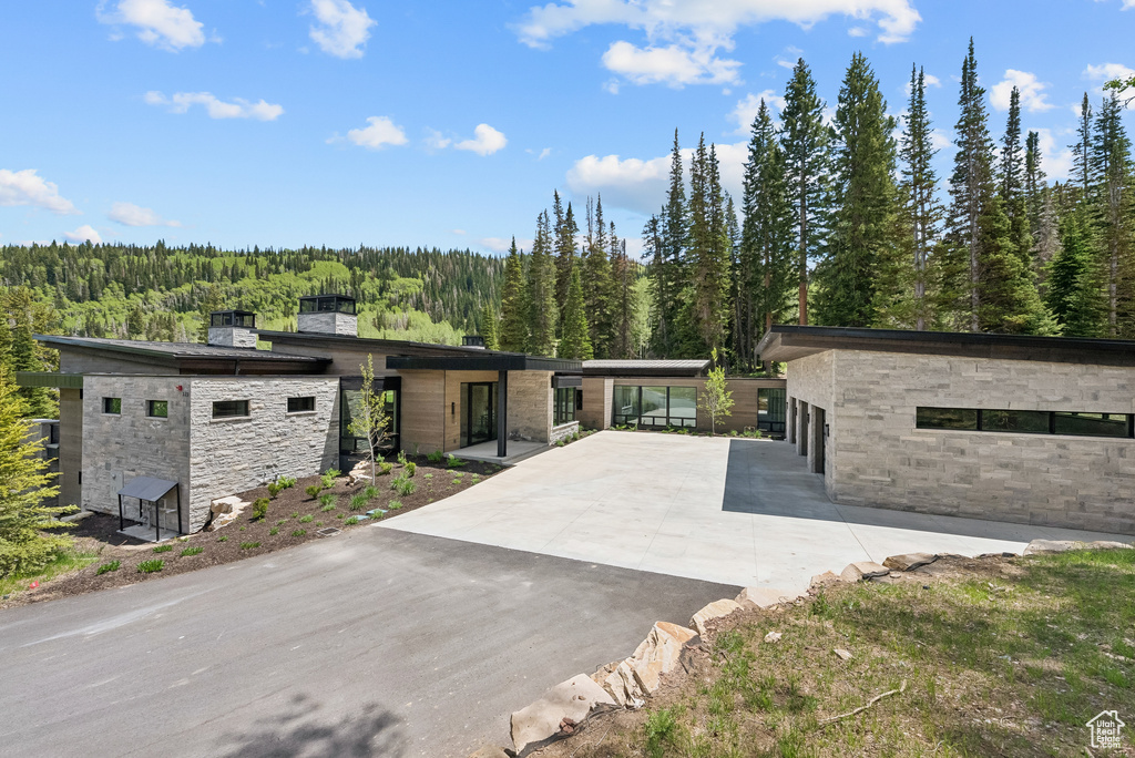 View of front of home with stone siding, a forest view, and concrete driveway