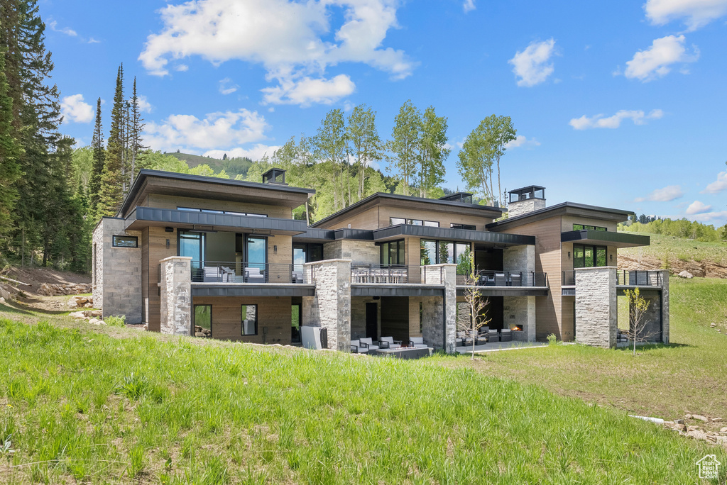 Back of house with a balcony, a chimney, and stone siding