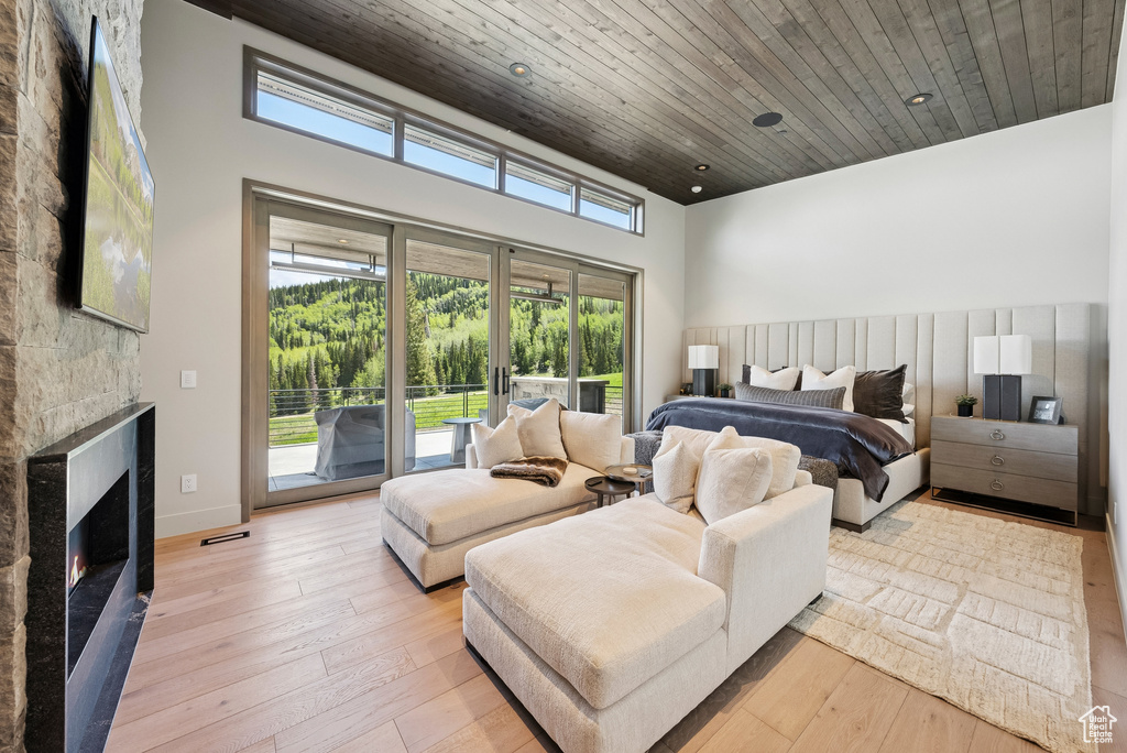 Bedroom with access to exterior, wooden ceiling, light wood-type flooring, a lit fireplace, and a high ceiling