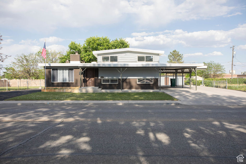 View of front of property featuring driveway, brick siding, a chimney, and a carport
