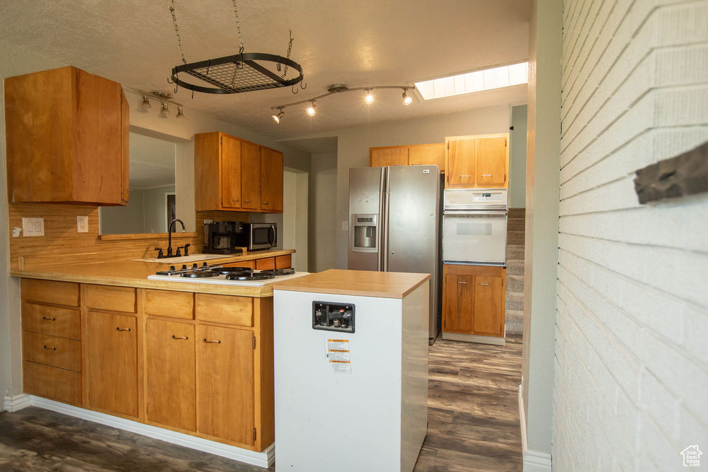 Kitchen featuring stainless steel appliances, dark wood-style floors, light countertops, track lighting, and a peninsula