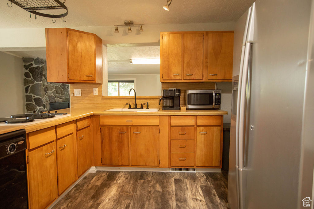 Kitchen with stainless steel appliances, dark wood finished floors, light countertops, backsplash, and brown cabinets