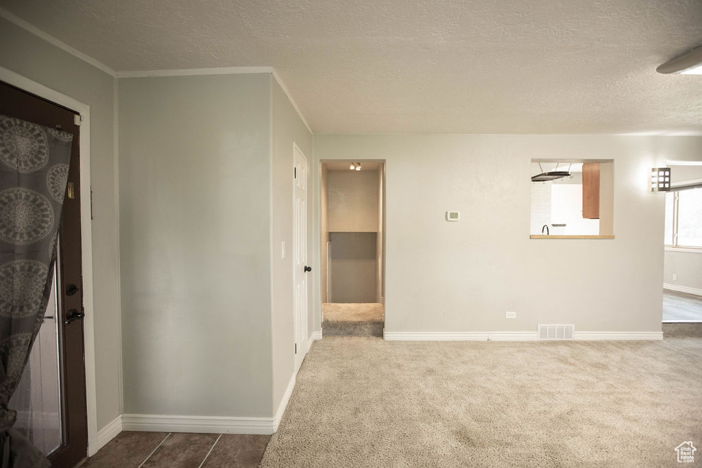 Unfurnished room featuring a textured ceiling, dark carpet, and crown molding