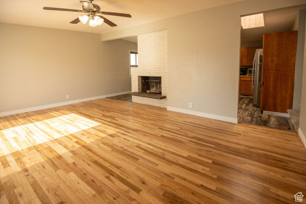 Unfurnished living room featuring wood finished floors, ceiling fan, and a fireplace
