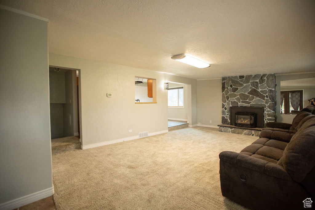 Carpeted living area featuring a textured ceiling and a stone fireplace