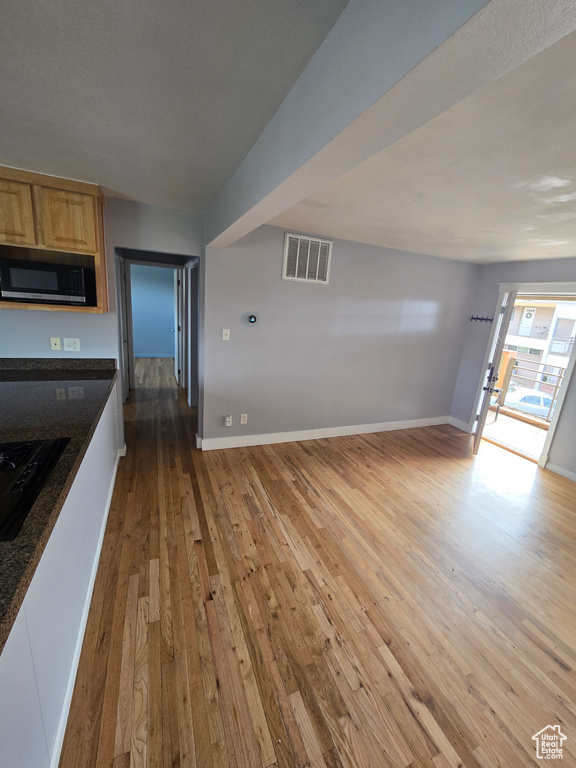 Kitchen with light wood finished floors, dark countertops, light brown cabinets, black gas cooktop, and open floor plan