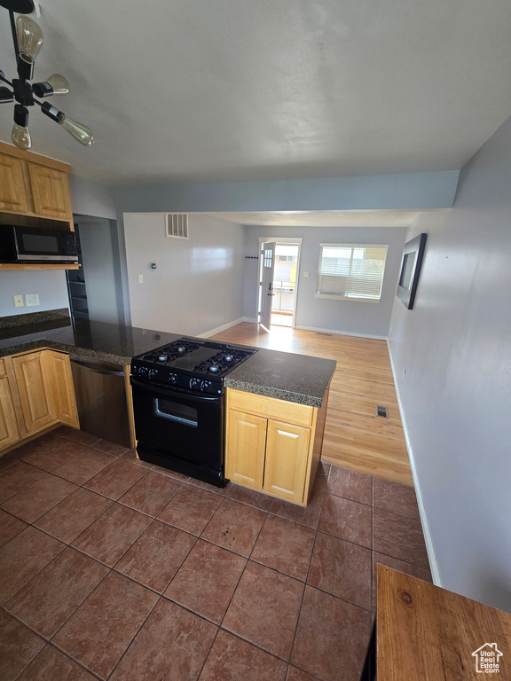Kitchen featuring black appliances, dark countertops, light brown cabinets, and dark tile patterned floors