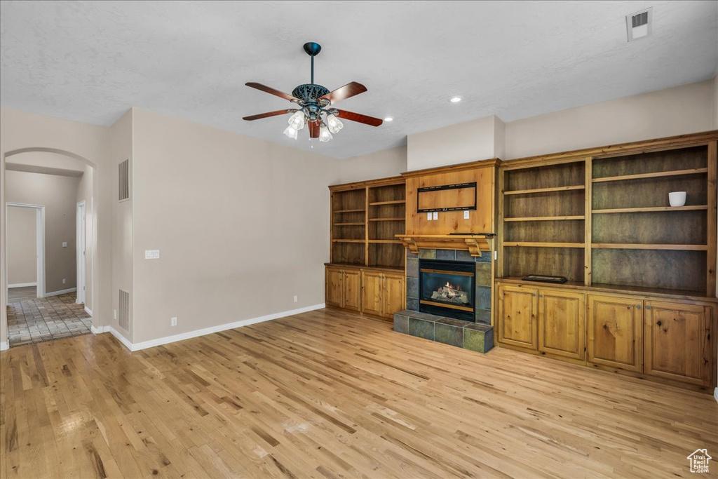 Unfurnished living room with arched walkways, light wood-style floors, a ceiling fan, a tile fireplace, and recessed lighting