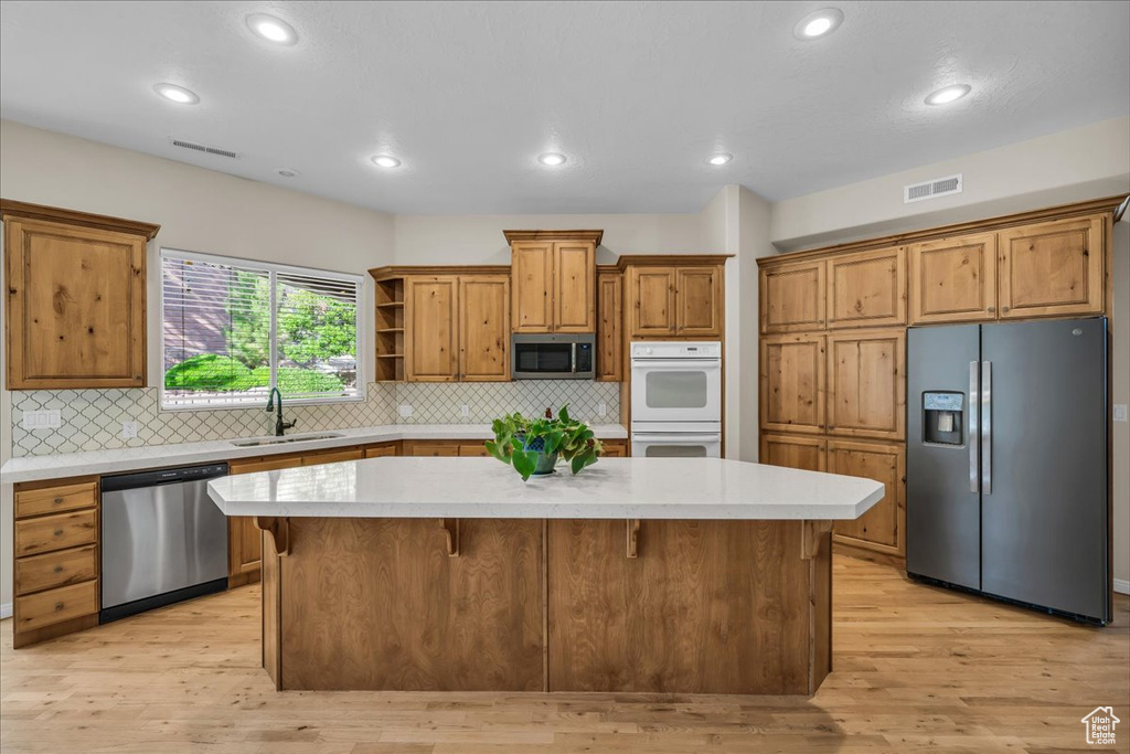Kitchen with appliances with stainless steel finishes, a center island, brown cabinetry, light countertops, and open shelves