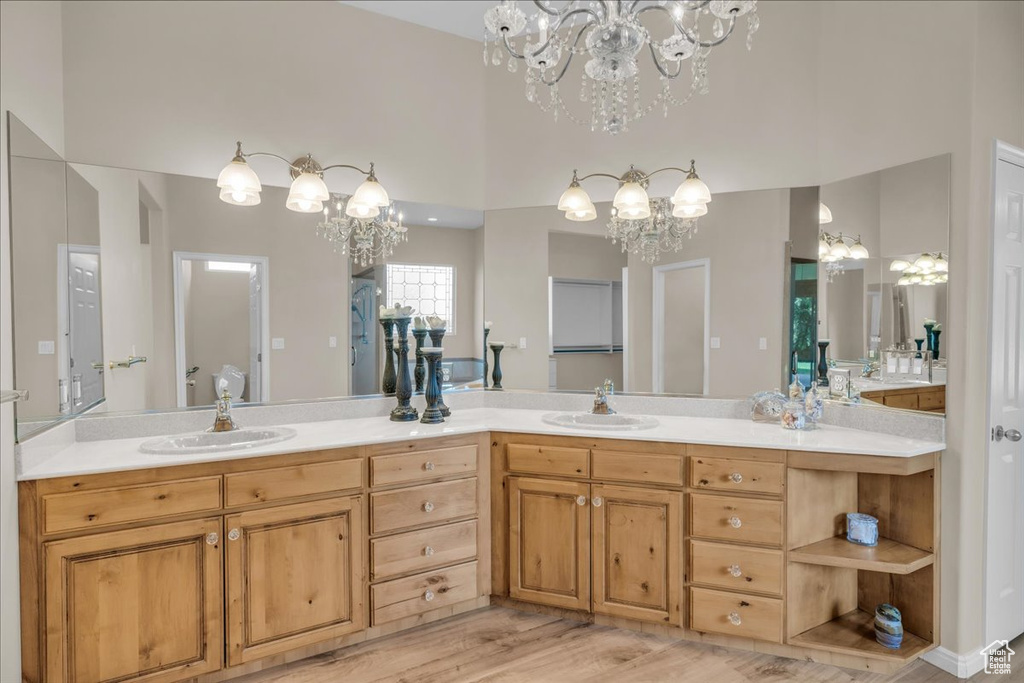 Full bath with a chandelier, double vanity, wood finished floors, and a high ceiling