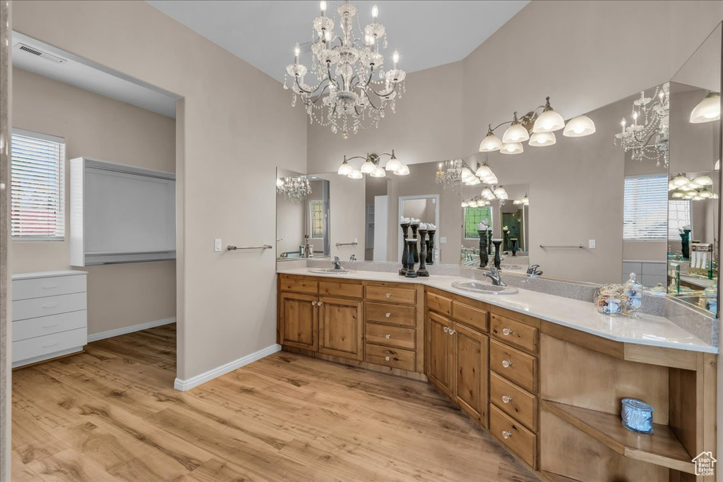 Full bath with a chandelier, double vanity, wood finished floors, and a high ceiling