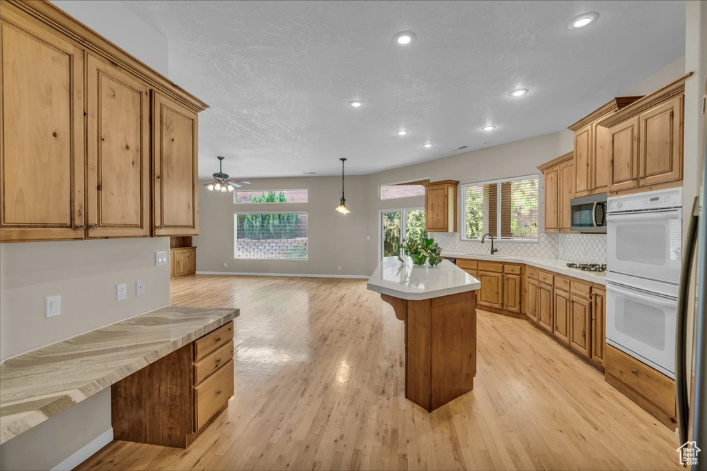 Kitchen featuring double oven, stainless steel microwave, light countertops, backsplash, and recessed lighting