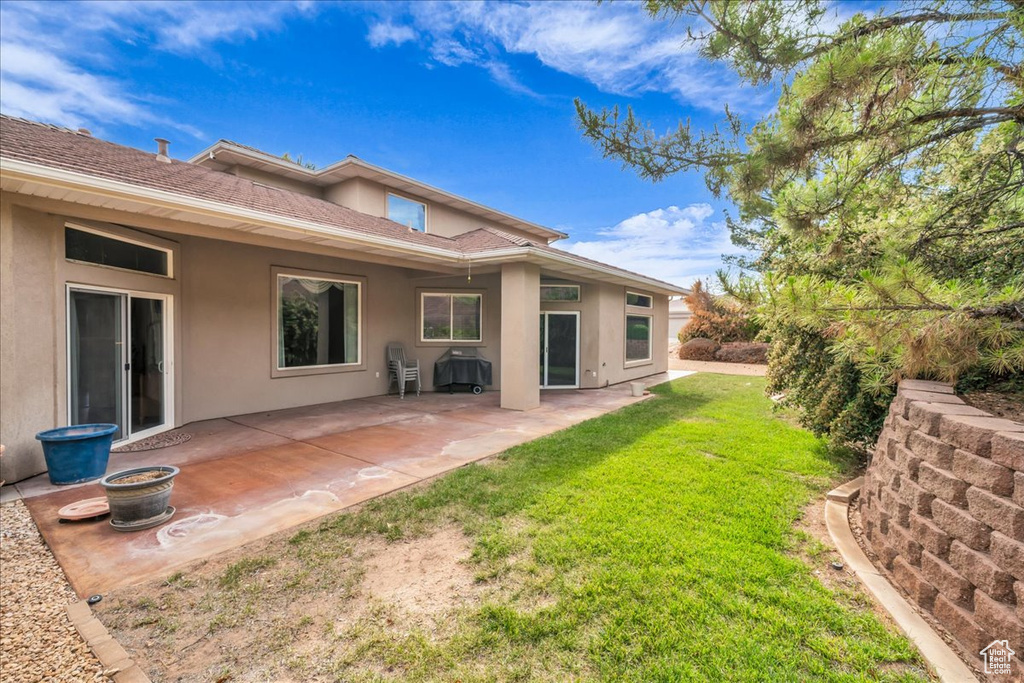 Back of house with stucco siding, a lawn, and a patio