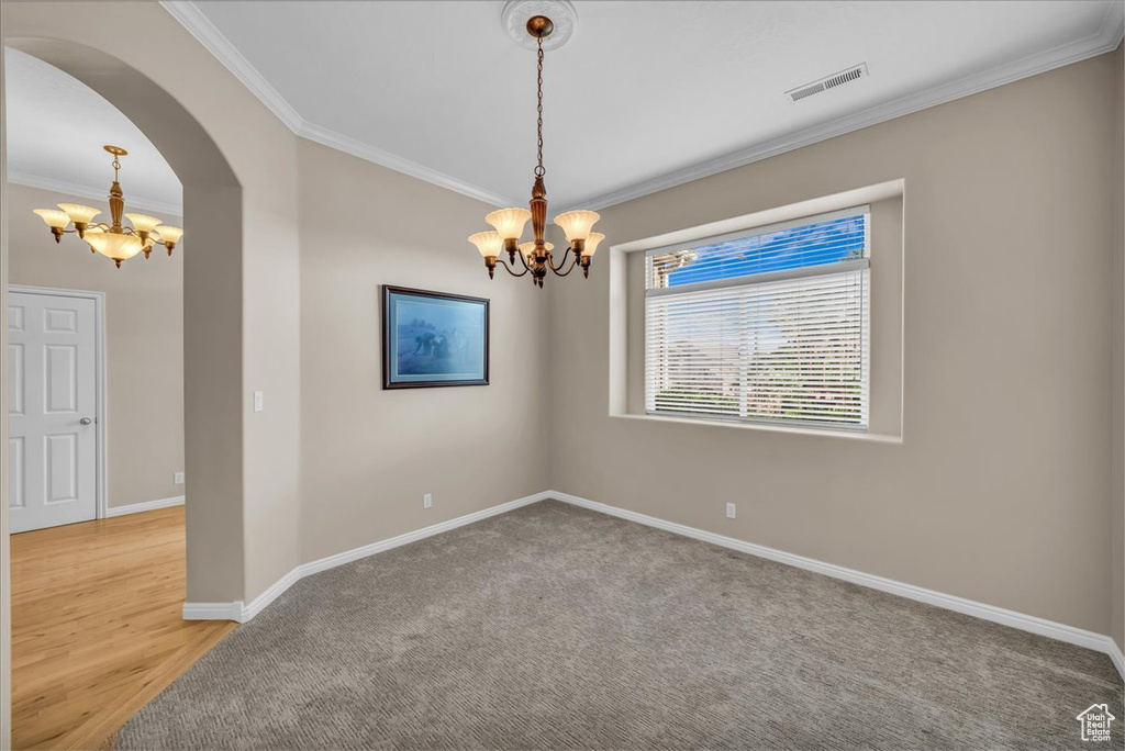 Spare room with a chandelier, crown molding, arched walkways, and light carpet