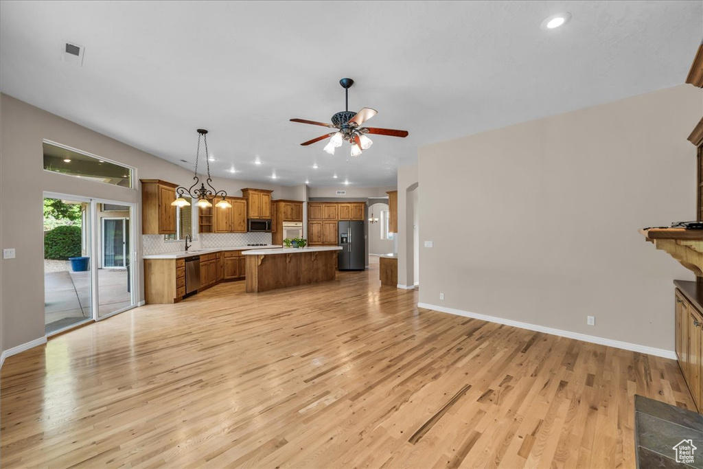 Kitchen with stainless steel appliances, brown cabinetry, open floor plan, light countertops, and light wood finished floors