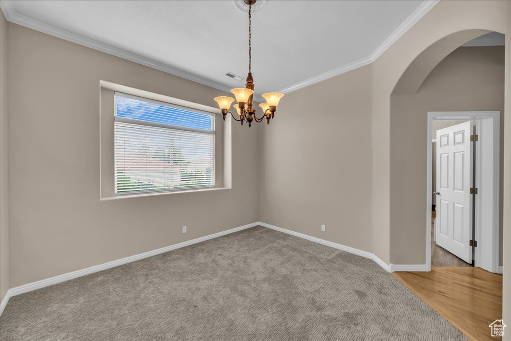 Spare room with crown molding, arched walkways, a chandelier, and carpet flooring