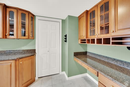 Kitchen with built in desk, dark stone counters, and glass insert cabinets