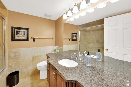 Bathroom featuring vanity, a shower with shower door, tile walls, and tile patterned floors