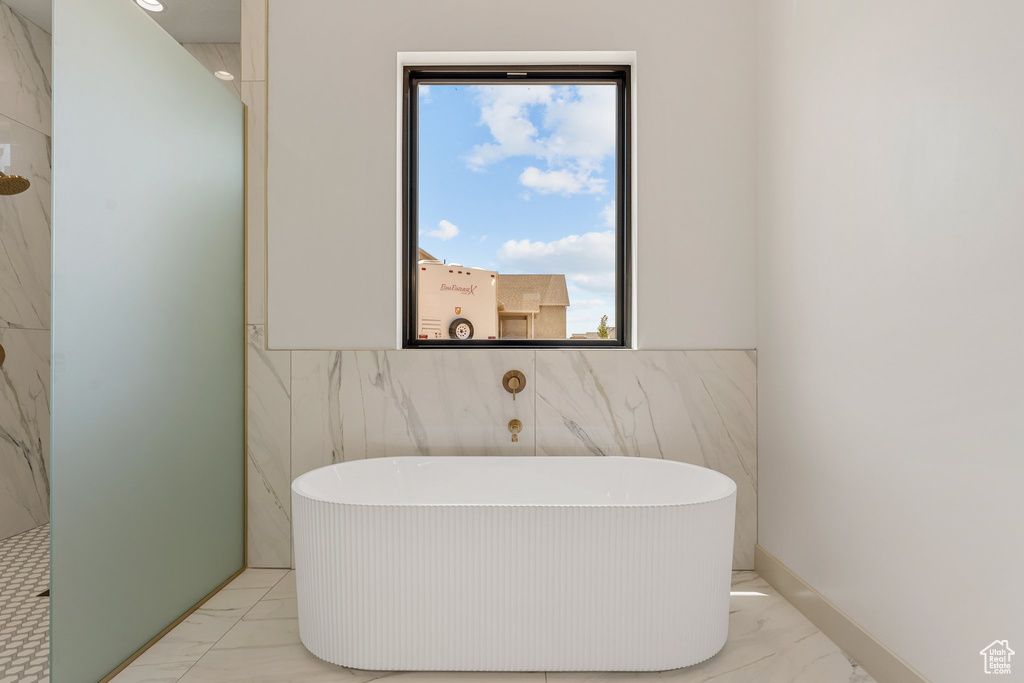 Bathroom featuring marble look tiles, tile walls, a freestanding bath, and a wainscoted wall
