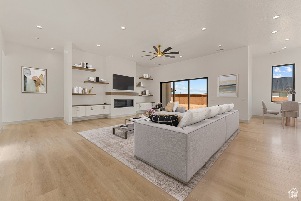 Living room featuring healthy amount of natural light, recessed lighting, light wood-style floors, a ceiling fan, and a glass covered fireplace