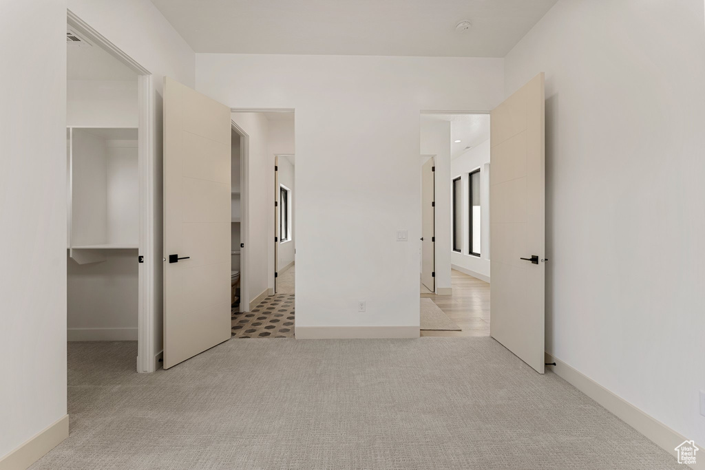 Unfurnished bedroom featuring light colored carpet, baseboards, and a walk in closet