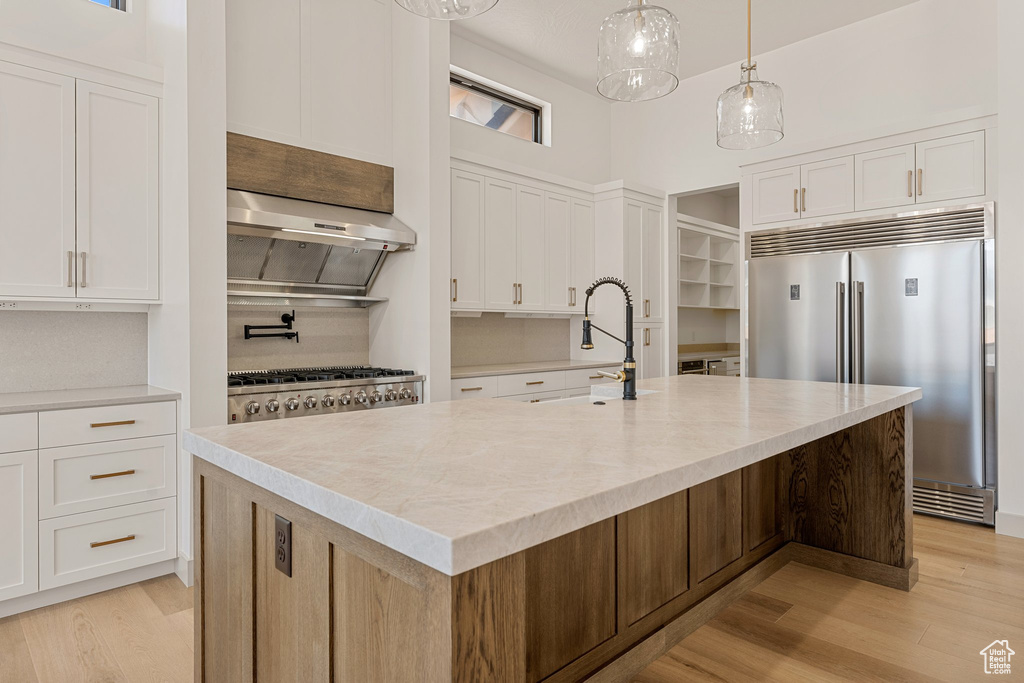 Kitchen featuring built in refrigerator, a sink, light wood-type flooring, white cabinetry, and an island with sink