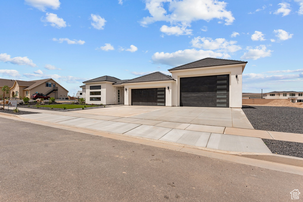 View of front of house with an attached garage, stucco siding, driveway, a tiled roof, and a residential view
