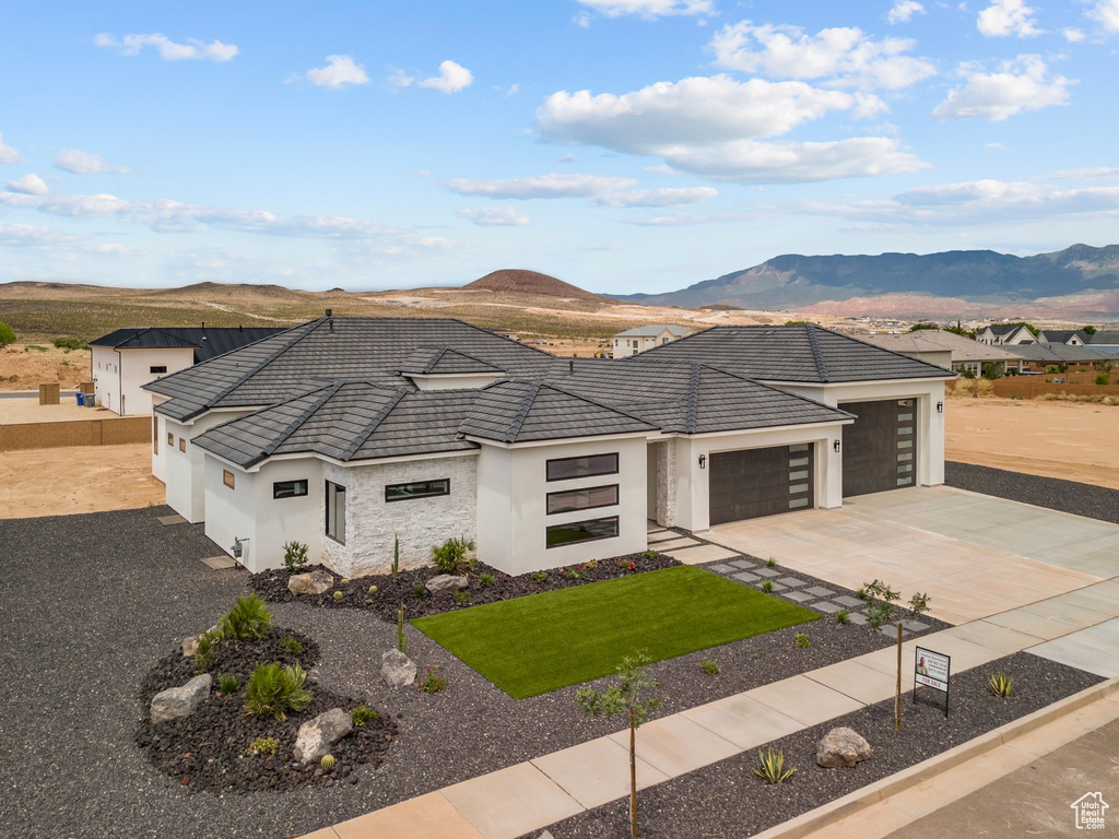 View of front of property featuring stucco siding, a garage, concrete driveway, a mountain view, and a front lawn