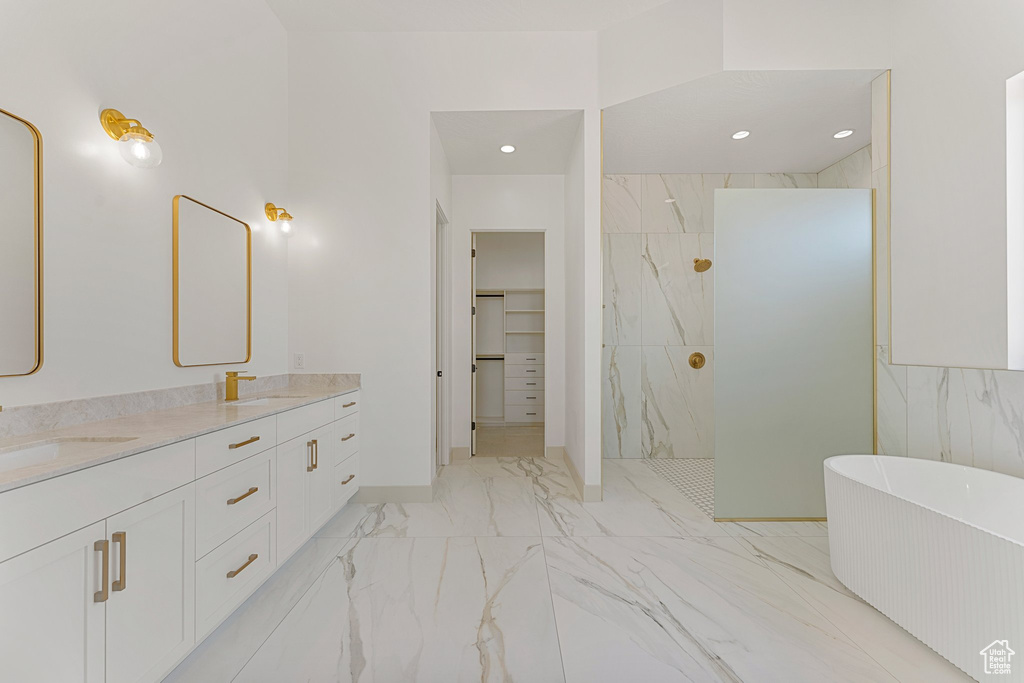 Full bath featuring a marble finish shower, double vanity, a soaking tub, marble look tiles, and a walk in closet