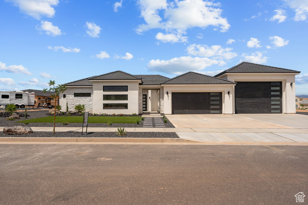 View of front facade featuring a garage, stucco siding, driveway, and a tile roof