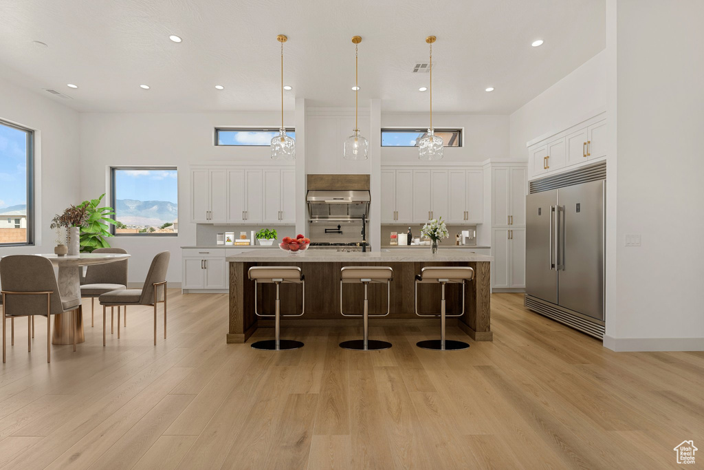 Kitchen featuring built in fridge, white cabinetry, light countertops, light wood-style floors, and a kitchen bar