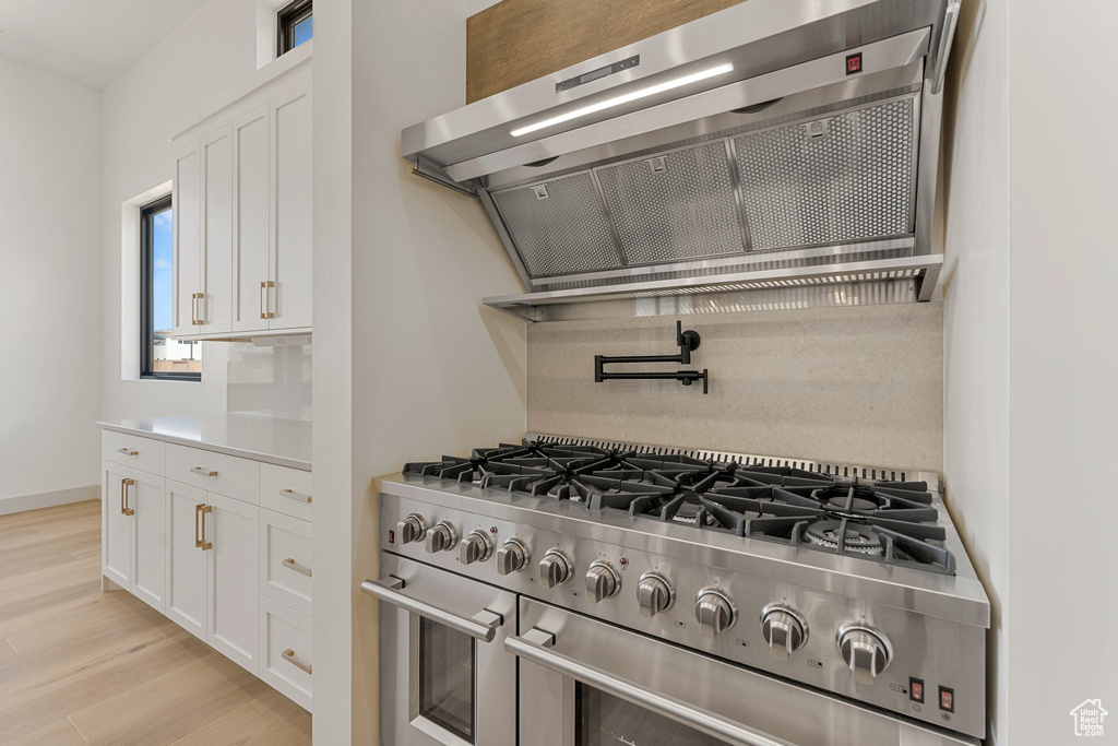 Kitchen with range with two ovens, range hood, white cabinets, light wood-style floors, and light countertops