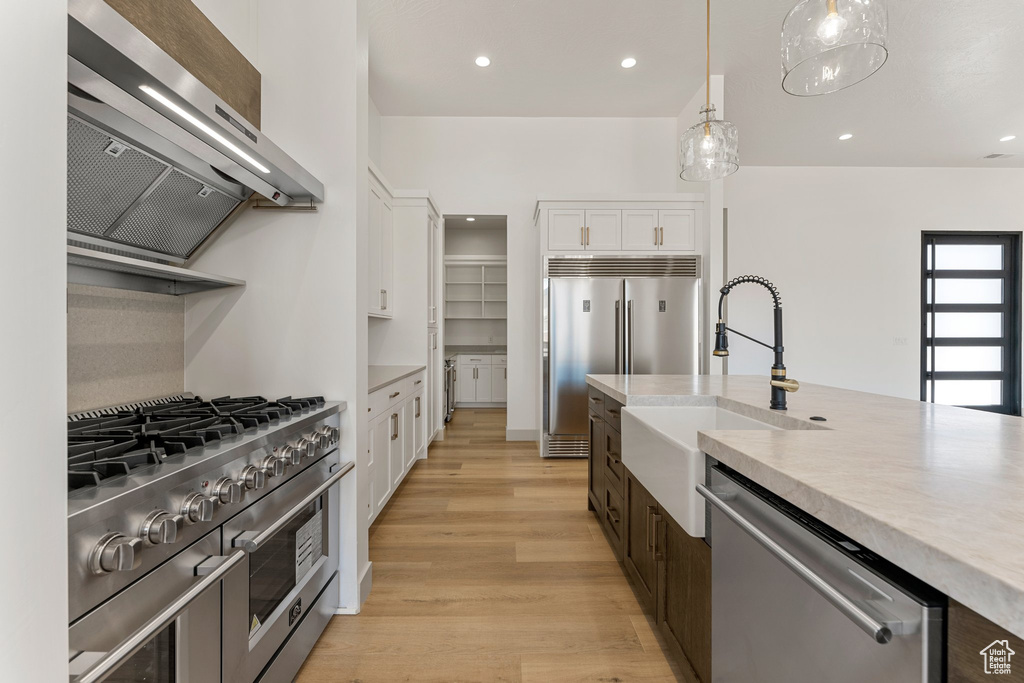 Kitchen with premium appliances, white cabinets, extractor fan, a sink, and light wood-style flooring