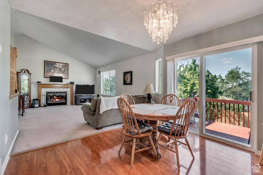 Dining space with hardwood / wood-style floors, a tiled fireplace, a chandelier, vaulted ceiling, and a textured ceiling