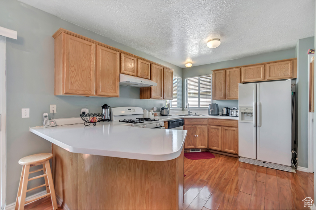 Kitchen with white appliances, under cabinet range hood, a peninsula, a textured ceiling, and light wood-style floors