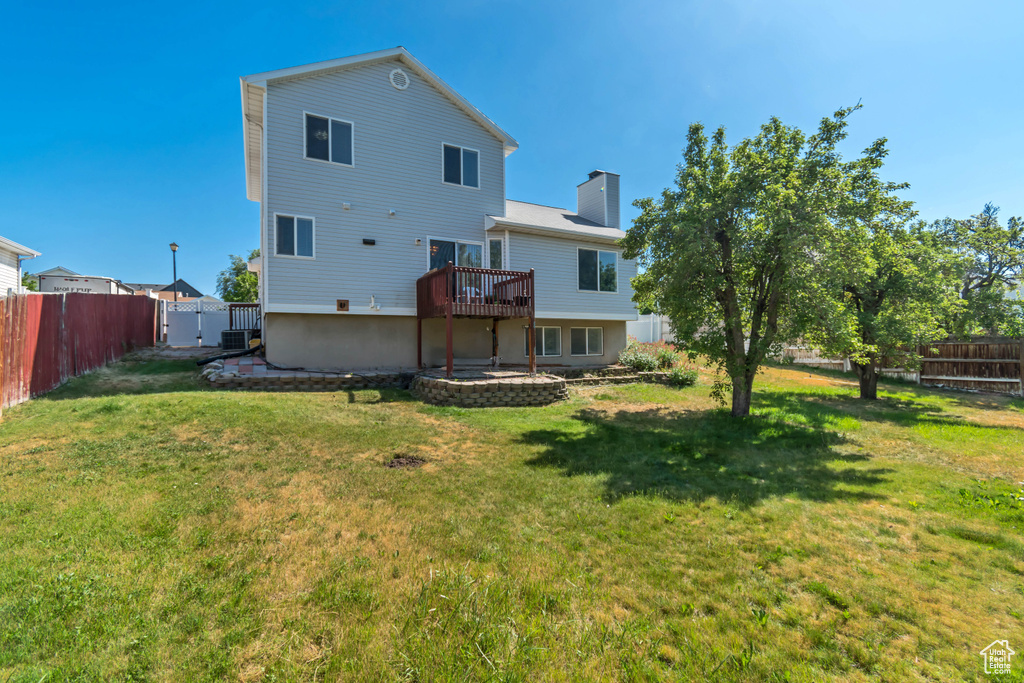 Back of property with a fenced backyard, a deck, and a chimney