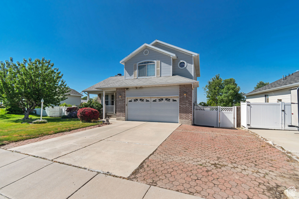 Traditional home with a gate, brick siding, a garage, and concrete driveway