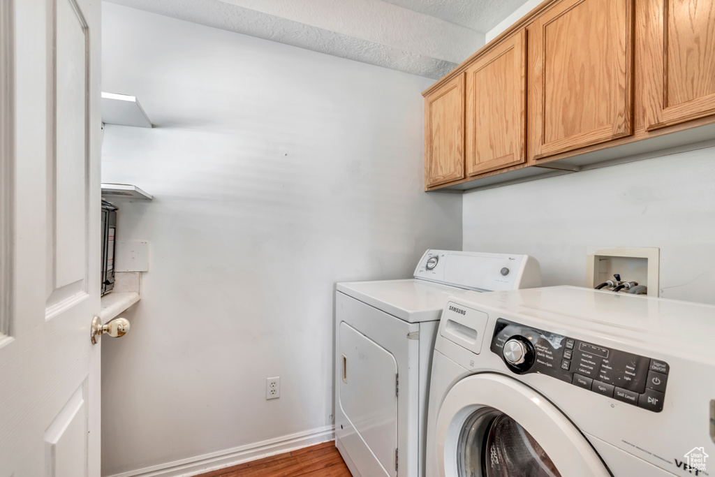 Washroom featuring independent washer and dryer, cabinet space, and wood finished floors