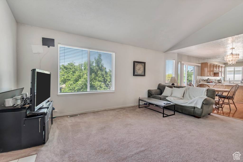 Living area featuring a chandelier, light colored carpet, and lofted ceiling