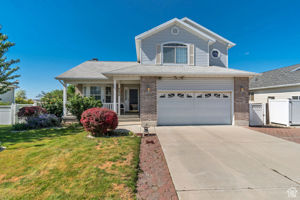 View of front of home featuring a gate, covered porch, brick siding, a garage, and concrete driveway