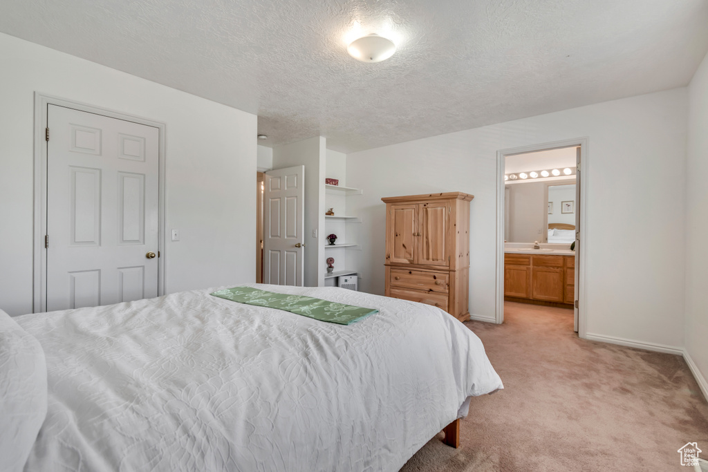 Bedroom with light carpet, a textured ceiling, and ensuite bath