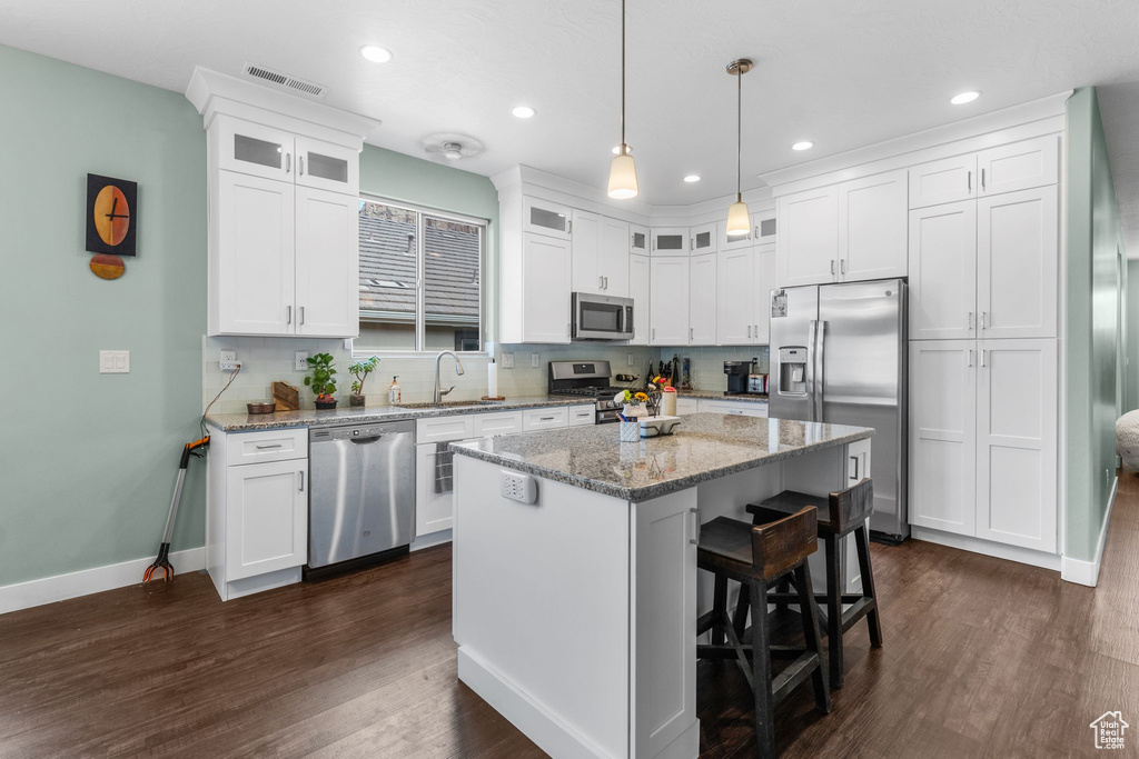 Kitchen featuring appliances with stainless steel finishes, white cabinetry, dark wood finished floors, a breakfast bar, and recessed lighting