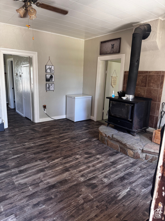 Living room with wood finished floors, a wood stove, and a ceiling fan