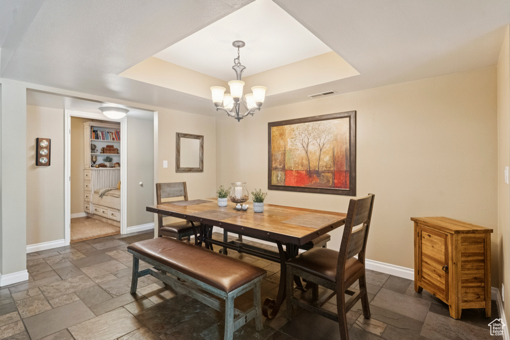 Dining area with stone tile floors, a tray ceiling, and a chandelier