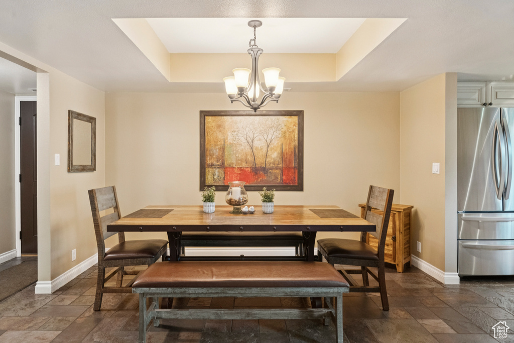 Dining space featuring stone tile flooring, a chandelier, and a raised ceiling