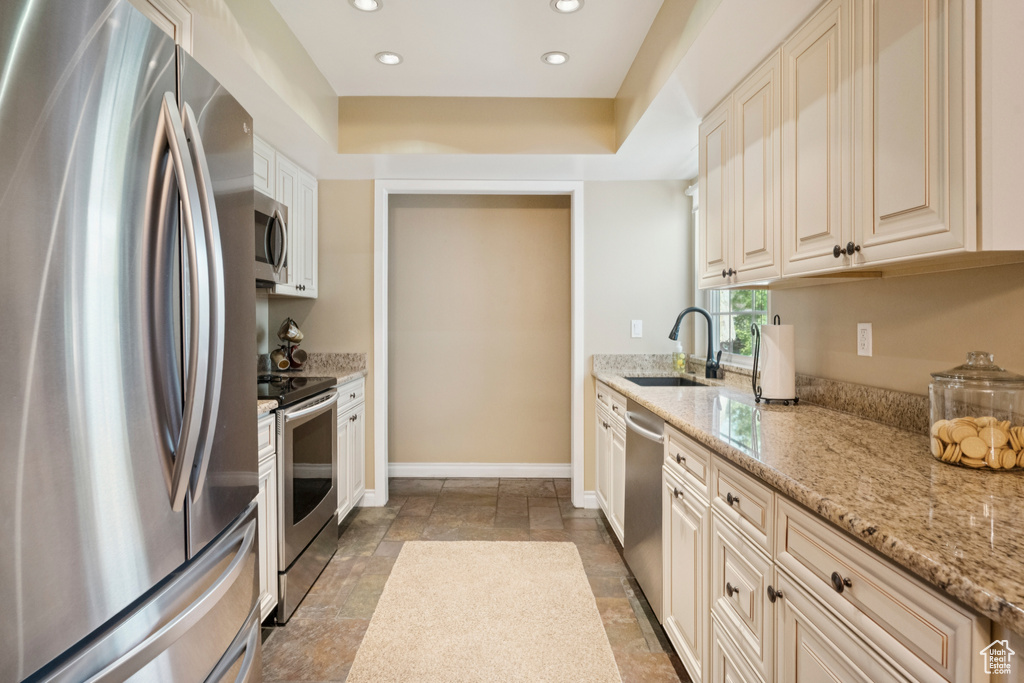 Kitchen with stainless steel appliances, stone tile flooring, recessed lighting, light stone countertops, and cream cabinets